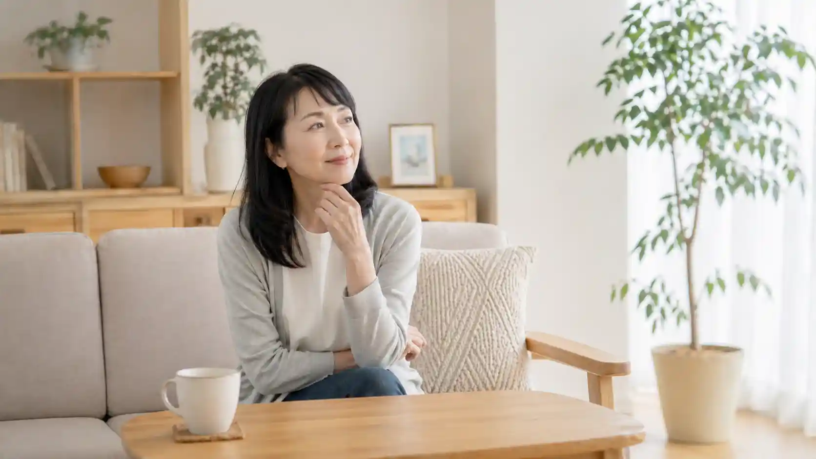 更年期の体の変化を感じながら、自然光の入る部屋で静かに座る40〜60代女性