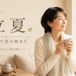 立夏の文字と、初夏の新緑を窓辺から眺めながら温かい飲み物を手に過ごす女性。暦の上で夏の始まりを表現した画像。