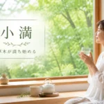 小満の文字と、初夏の新緑を窓辺から眺めながら水分をとる女性。草木が満ち始める頃の穏やかな養生を表現した画像。